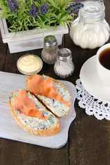 Fish sandwiches and cup of tea on cutting board on wooden table