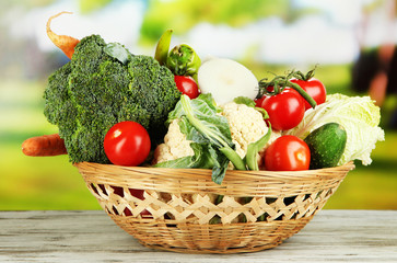 Fresh vegetables in basket on wooden table on natural
