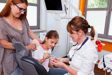 A doctor explains mother and douther how they can care the teeth