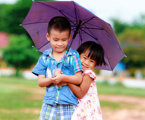 A smiling boy and a little girl with umbrella in the park