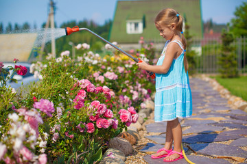 ?ute girl in blue dress watering flowers with a hose in her
