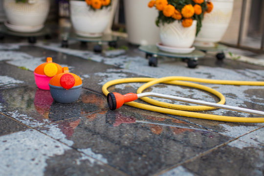 Children's bright watering can and a long hose on the wet ground