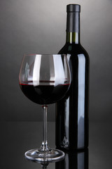 Red wine glass and bottle of wine on grey background