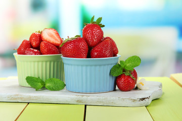 Ripe sweet strawberries in bowls on green wooden table
