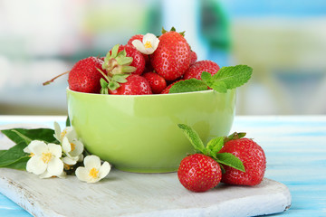 Ripe sweet strawberries in green bowl on blue wooden table
