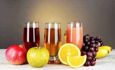 Glasses of fresh juice on table on gray background