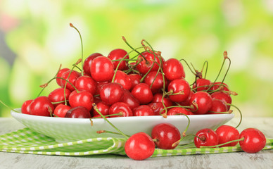 Cherry berries on plate on wooden table on bright background