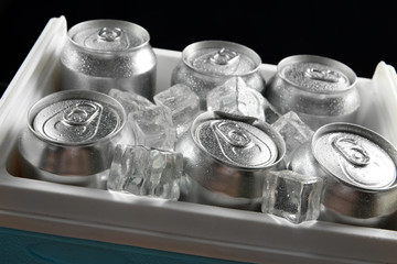 Metal cans of beer with ice cubes in mini refrigerator, close