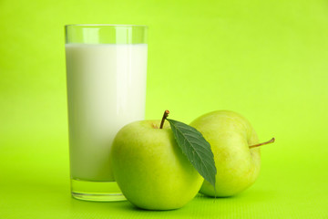 Glass of kefir and apples, on green background