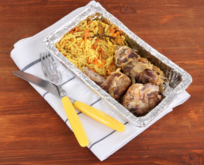 Food in box of foil on napkin on wooden background