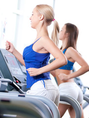 Fototapeta na wymiar Two young women run on machine in the gym