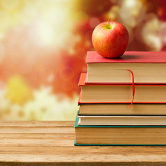 Old vintage books and apple over autumn leaves bokeh background