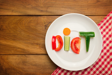 Plate with vegetables and word diet over wooden background