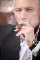 Smoking a cigar. Successful mature businessman smoking a cigar a