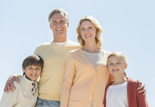 Happy Family Of Four Standing Against Clear Blue Sky