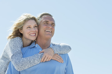 Woman Embracing Man From Behind While Looking Away Against Sky