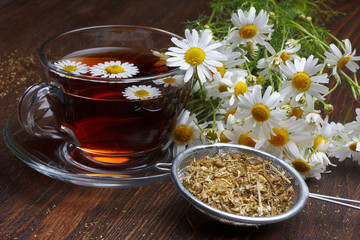 Chamomile tea and dried flowers on wooden table