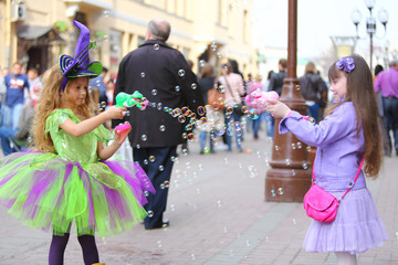 little girls blow soap bubbles in street on holiday