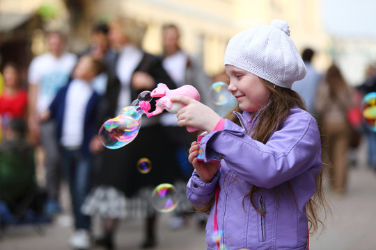 girl is playing with soap bubbles gun on holiday of spring