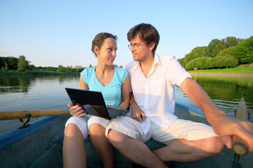 Young couple floating down river on boat with oars with laptop