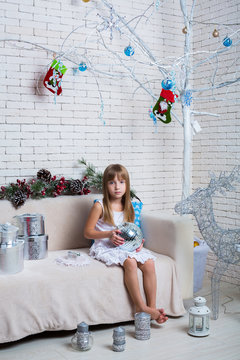Little girl sitting on sofa with Christmas gifts and mirror ball