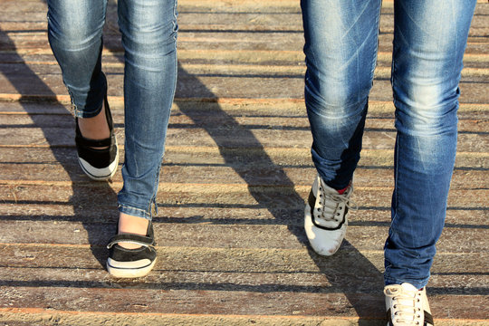 female legs in jeans and sneakers closeup on wooden background