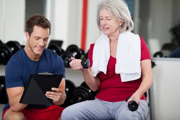 Fotobehang Persoonlijk trainer berät seniorin im fitnessstudio  © contrastwerkstatt