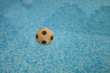 Fototapeta na wymiar Floating football in a swimming pool with blue tiles