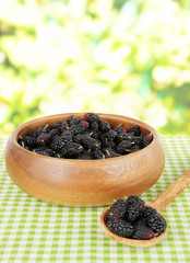 Ripe mulberries in bowl on table on bright background