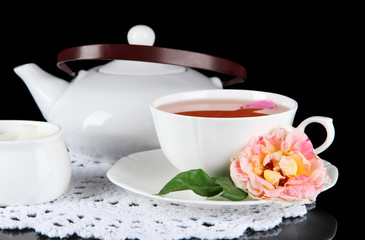 Kettle and cup of tea from tea rose on napkin black background