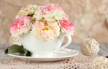 Roses in cup on napkins on  wooden table on beige background