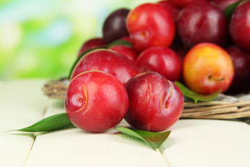Ripe plums in basket on wooden table on natural background