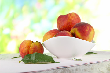 Peaches in plate on napkin on wooden table on nature background