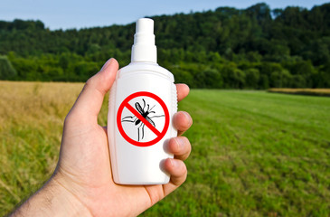 Hand hält Spraydose mit Anti Mücken Spray draußen auf grüner Wiese/Feld