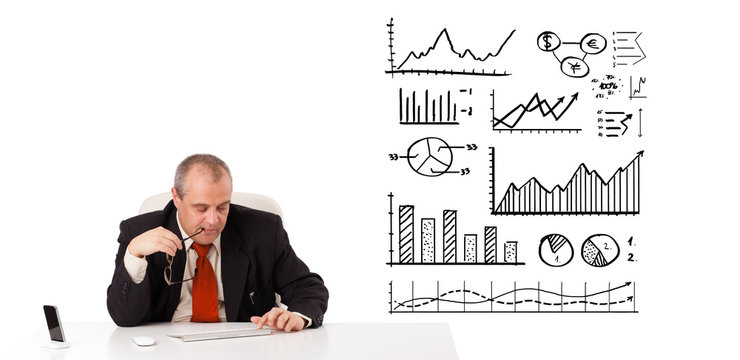 Businessman sitting at desk with diagrams and graphs