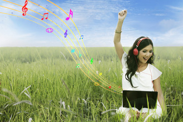 Attractive female listening to music on green field