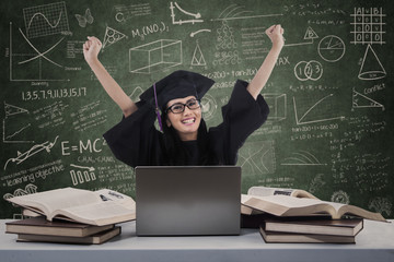 Cheerful graduate with laptop in class