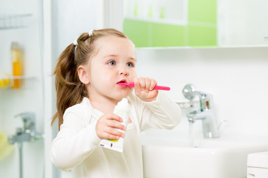 Child girl brushing teeth in bathroom