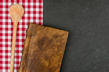 Kochlöffel und Kochbuch auf einer Schieferplatte 