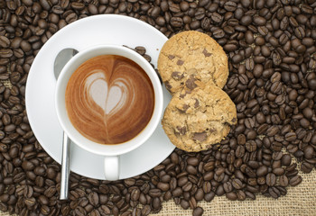 Cup of coffee with heart shape in foam on hessian background