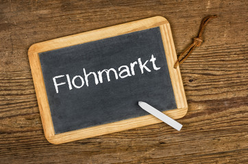 Leere Schiefertafel mit dem Text Flohmarkt auf einem Holztisch
