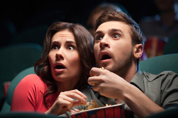 Horror movie. Terrified young couple eating popcorn while watchi