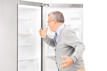 Fototapeta na wymiar Shocked mature man looking in empty fridge and finding out there
