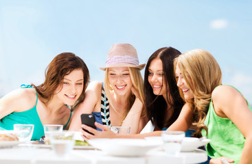 girls looking at smartphone in cafe on the beach