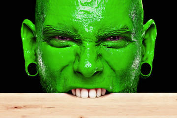 Mann mit grünem Gesicht beißt in die Tischkante