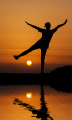 Silhouette woman jumping against orange sunset