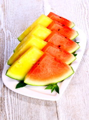 Red and yellow watermelon with mint on white plate