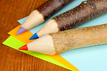 Colorful wooden pencils with sheets of paper on wooden table