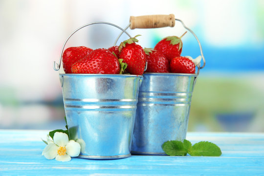 Ripe sweet strawberries in metal pails on blue wooden table
