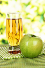 Glass of fresh apple juice on table on bright background